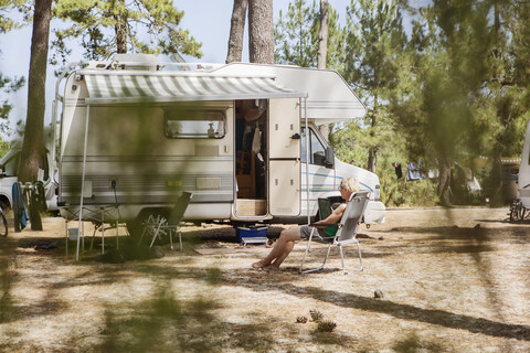 Frankreich, Gironde, Frau sitzt vor einem Wohnwagen auf einem Campingplatz und benutzt ein Tablet, lizenzfreies Stockfoto