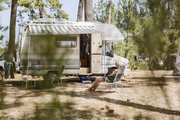 Frankreich, Gironde, Frau sitzt vor einem Wohnwagen auf einem Campingplatz und benutzt ein Tablet - JATF01132