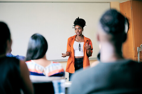 Selbstbewusste junge Frau gestikuliert, während sie Schüler unterrichtet, lizenzfreies Stockfoto