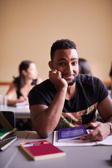 Porträt eines selbstbewussten Mannes mit Buch am Schreibtisch im Klassenzimmer - MASF11258