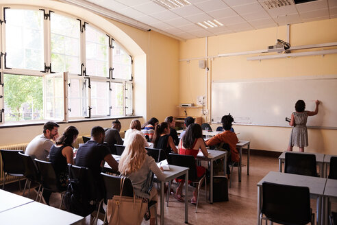 Lehrer schreibt auf der Tafel, während die Schüler im Klassenzimmer sitzen - MASF11270