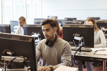 Seriöser junger Mann an einem Computer mit Studenten im Hintergrund in einer Bibliothek - MASF11289