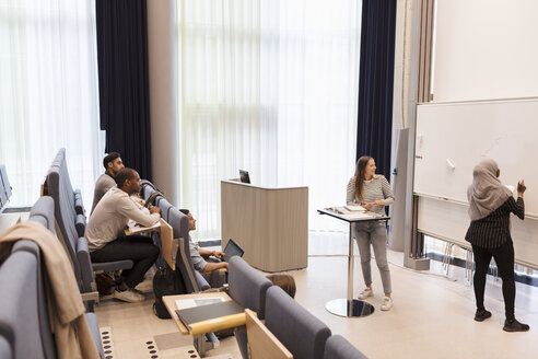 Studenten betrachten einen Freund, der während einer Probe im Hörsaal auf die Tafel schreibt - MASF11293