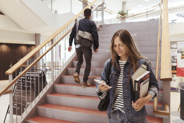 Eine Studentin benutzt ein Mobiltelefon, während ein Mann auf einer Treppe in der Universität nach oben geht - MASF11305