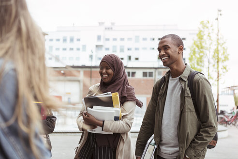 Lächelnde männliche und weibliche Studenten stehen mit Freunden auf dem Universitätscampus - MASF11307