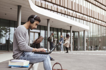 Junge Studentin hört Musik, während sie einen Laptop auf dem Universitätscampus benutzt - MASF11316