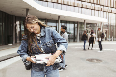 Lächelnde junge Frau mit Büchern in der Hand auf dem Universitätscampus - MASF11320