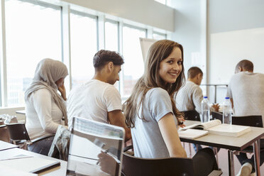 Porträt eines lächelnden Schülers, der mit Freunden im Klassenzimmer einer High School sitzt - MASF11324