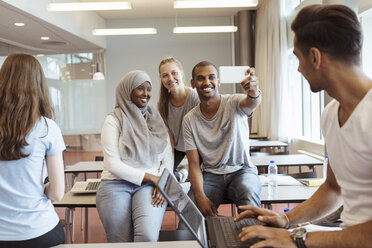 Students looking at friends taking selfie in university classroom - MASF11326