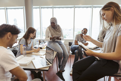 Lächelnde multiethnische Freunde, die in einem Klassenzimmer an der Universität über ein Projekt diskutieren - MASF11332