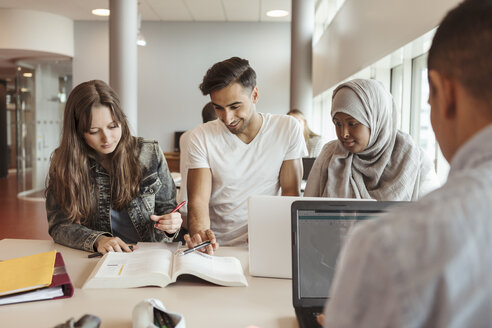 Multiethnische Freunde lesen ein Lehrbuch am Schreibtisch in der Universität - MASF11334