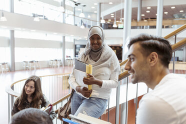 Lächelnde Frau im Hidschab mit Freunden auf den Stufen eines Universitätsgeländes - MASF11340