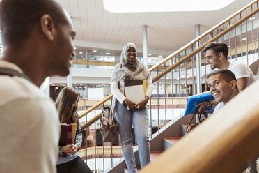 Lächelnde männliche und weibliche Studenten, die auf einer Treppe diskutieren - MASF11342