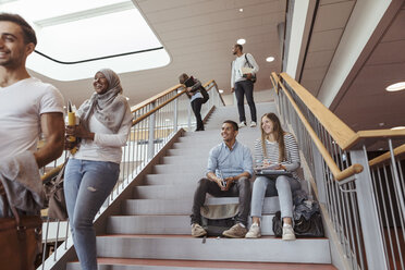 Lächelnde Studenten, die auf den Stufen sitzen und ihre Freunde in der Universität betrachten - MASF11343