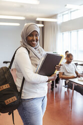Porträt einer lächelnden Frau im Hidschab, die mit Büchern in einem Universitätsklassenzimmer steht - MASF11350