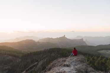 Spain, Gran Canaria, Pico de las Nieves, back view of woman sitting on rock looking at view - KKAF03117