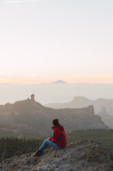 Spanien, Gran Canaria, Pico de las Nieves, Frau sitzt auf einem Felsen und betrachtet die Aussicht - KKAF03118