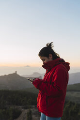 Spain, Gran Canaria, Pico de las Nieves, young woman using smartphone - KKAF03121