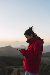 Spanien, Gran Canaria, Pico de las Nieves, junge Frau mit Smartphone - KKAF03121
