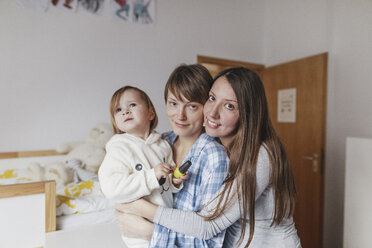 Porträt eines glücklichen lesbischen Paares, das seine Tochter zu Hause umarmt - KMKF00760