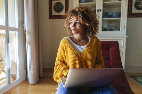 Young woman sitting on chaiselongue using laptop at home - KIJF02273