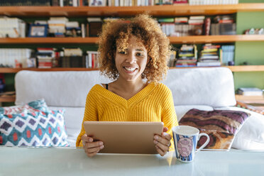 Portrait of smiling young woman with curly hair using tablet at home - KIJF02279