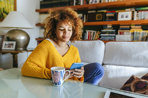 Young woman with curly hair using cell phone at home stock photo