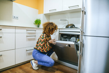 Young woman with curly opening the dishwasher in kitchen - KIJF02296