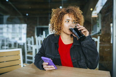 Junge Frau mit Handy trinkt Cola in einer Bar - KIJF02323