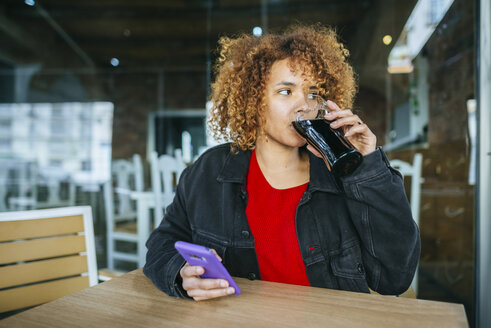 Junge Frau mit Handy trinkt Cola in einer Bar - KIJF02323