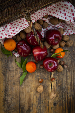 Weidenkorb, rote Äpfel, Mandarinen, Haselnüsse und Walnüsse auf dunklem Holz, lizenzfreies Stockfoto