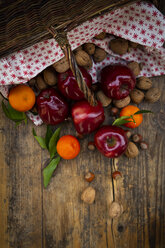 Weidenkorb, rote Äpfel, Mandarinen, Haselnüsse und Walnüsse auf dunklem Holz - LVF07789