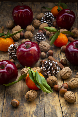 Rote Äpfel, Mandarinen, Haselnüsse, Walnüsse, Zimtstangen und Tannenzapfen auf dunklem Holz, lizenzfreies Stockfoto