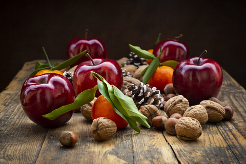 Rote Äpfel, Mandarinen, Haselnüsse, Walnüsse und Pinienzapfen auf dunklem Holz, lizenzfreies Stockfoto