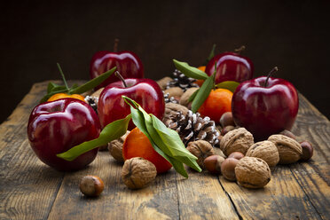 Rote Äpfel, Mandarinen, Haselnüsse, Walnüsse und Pinienzapfen auf dunklem Holz - LVF07792