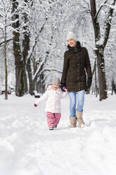 Glückliche Mutter, die mit ihrer Tochter in einer Winterlandschaft spazieren geht - DIGF05861