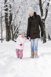 Glückliche Mutter, die mit ihrer Tochter in einer Winterlandschaft spazieren geht - DIGF05862