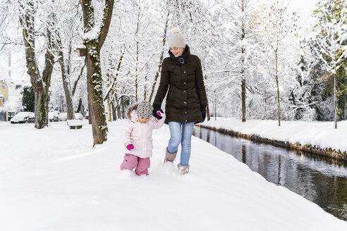 Glückliche Mutter, die mit ihrer Tochter an einem Wassergraben in einer Winterlandschaft spazieren geht - DIGF05863