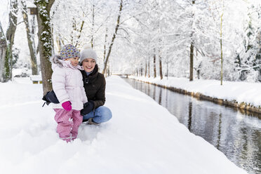 Glückliche Mutter mit Tochter an einem Wassergraben in Winterlandschaft - DIGF05870