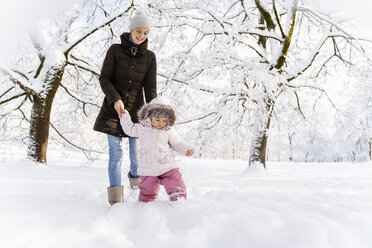 Glückliche Mutter, die mit ihrer Tochter in einer Winterlandschaft spazieren geht - DIGF05880