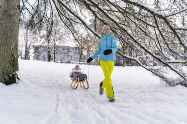 Glückliche Mutter mit Tochter auf Schlitten in Winterlandschaft - DIGF05900