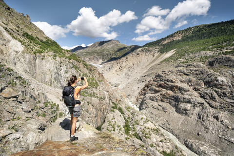 Schweiz, Wallis, Frau beim Fotografieren während einer Wanderung in den Bergen am Aletschgletscher, lizenzfreies Stockfoto