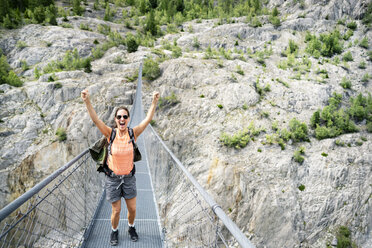 Switzerland, Valais, cheering woman on a hiking trip in the mountains from Belalp to Riederalp on a swinging bridge - DMOF00118