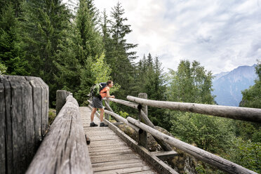 Switzerland, Valais, woman standing on a wooden bridge during a hiking trip on the Massaweg in the mountains - DMOF00119