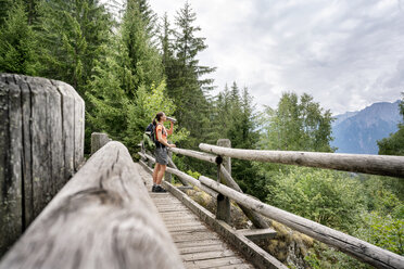 Schweiz, Wallis, Frau steht auf einer Holzbrücke während einer Wanderung auf dem Massaweg in den Bergen - DMOF00120