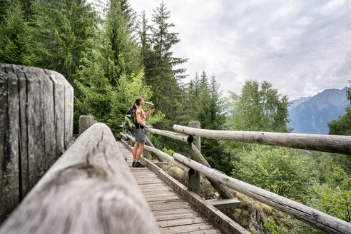 Schweiz, Wallis, Frau steht auf einer Holzbrücke während einer Wanderung auf dem Massaweg in den Bergen - DMOF00120