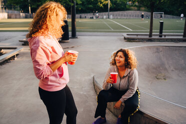 Lächelnde junge Frauen unterhalten sich bei einem Drink im Skateboardpark - MASF11370