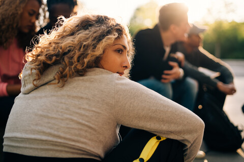 Nachdenkliche Frau sitzt mit Freunden im Skateboardpark, lizenzfreies Stockfoto