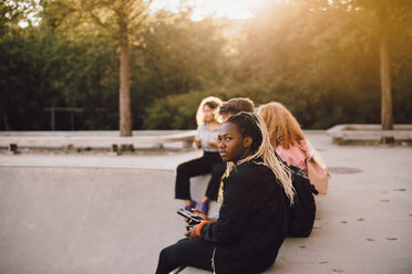 Nachdenkliches Teenager-Mädchen, das sein Handy in der Hand hält, während es mit Freunden im Skateboard-Park sitzt - MASF11386