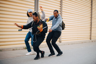 Volle Länge von Freunden tanzen auf dem Bürgersteig durch Fensterladen in der Stadt - MASF11395